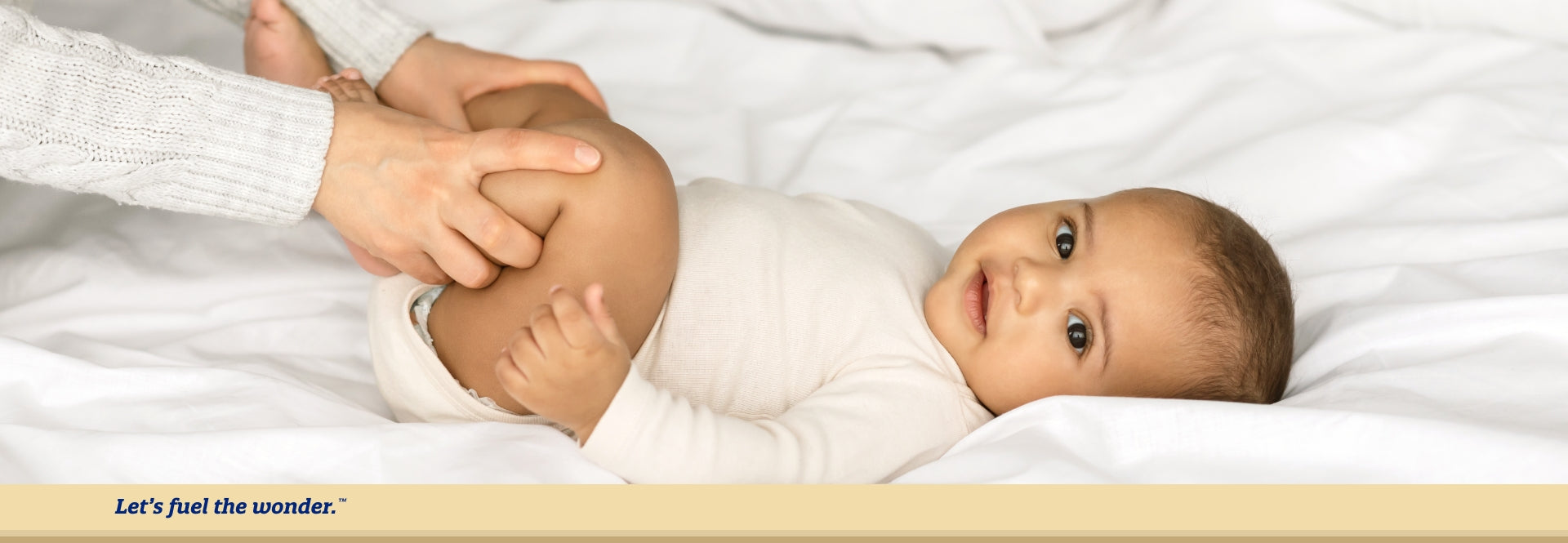 baby laying on back in bed while parent is holding baby's legs up and together to help with gas