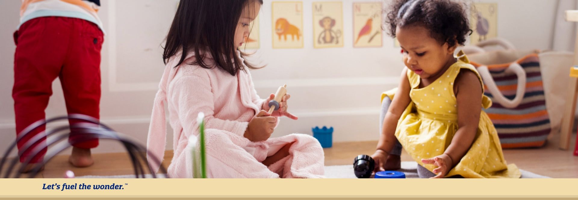 Two toddlers sitting on the ground looking down and facing each  other while playing with toys
