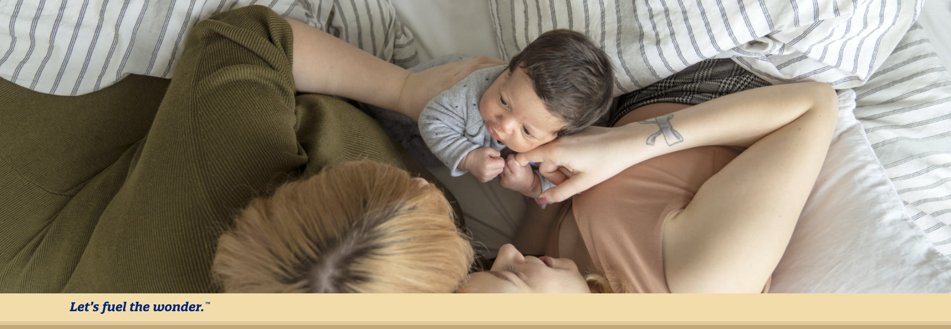 Partners laying in bed playing with sitting baby
