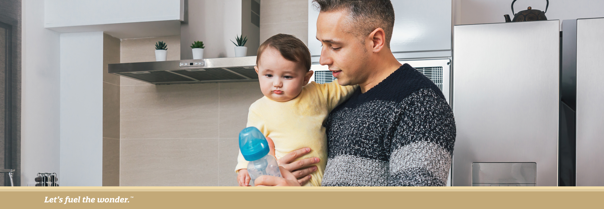 Father holding baby in kitchen while preparing a bottle.