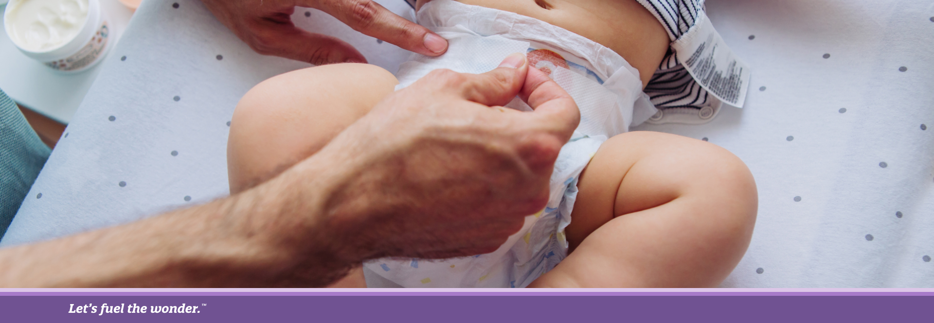 Caregiver changing a baby's diaper on a changing pad with diaper cream nearby