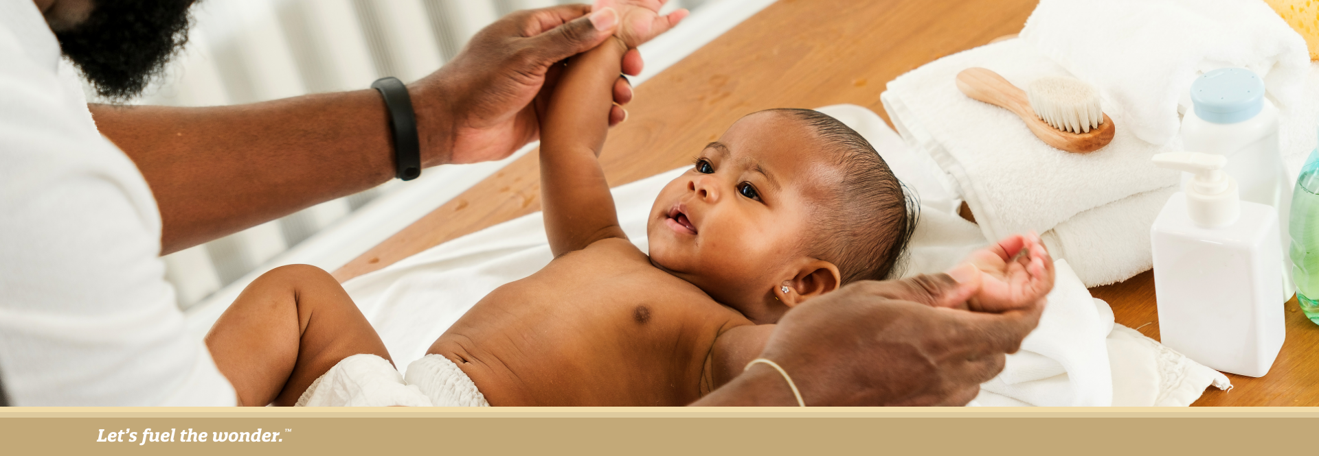 Father gently holding his baby’s arms while changing a diaper on a wooden changing table.