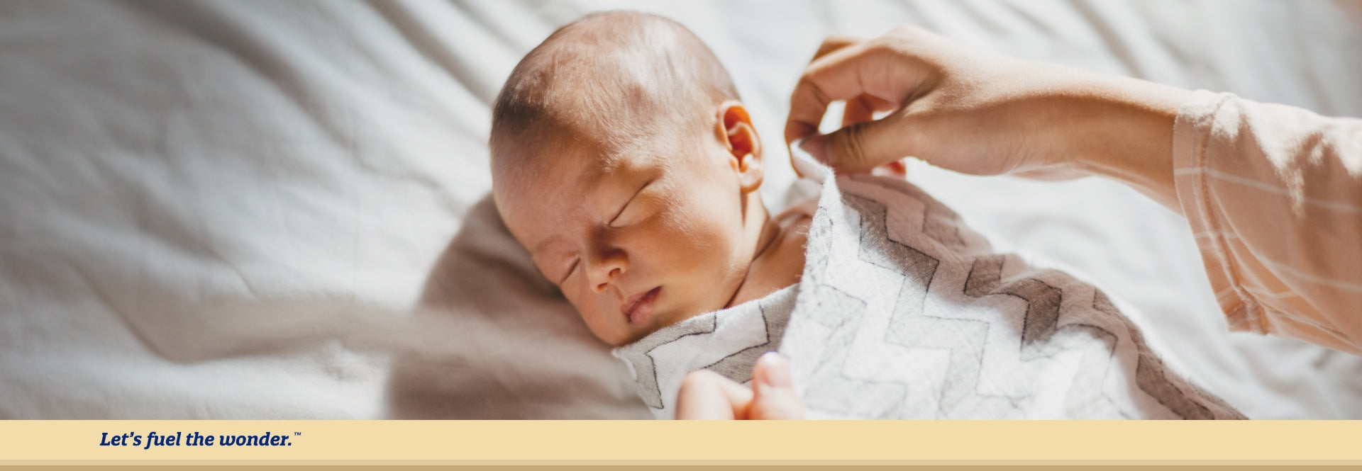 sleeping baby laying on bed while parent places swaddle around baby