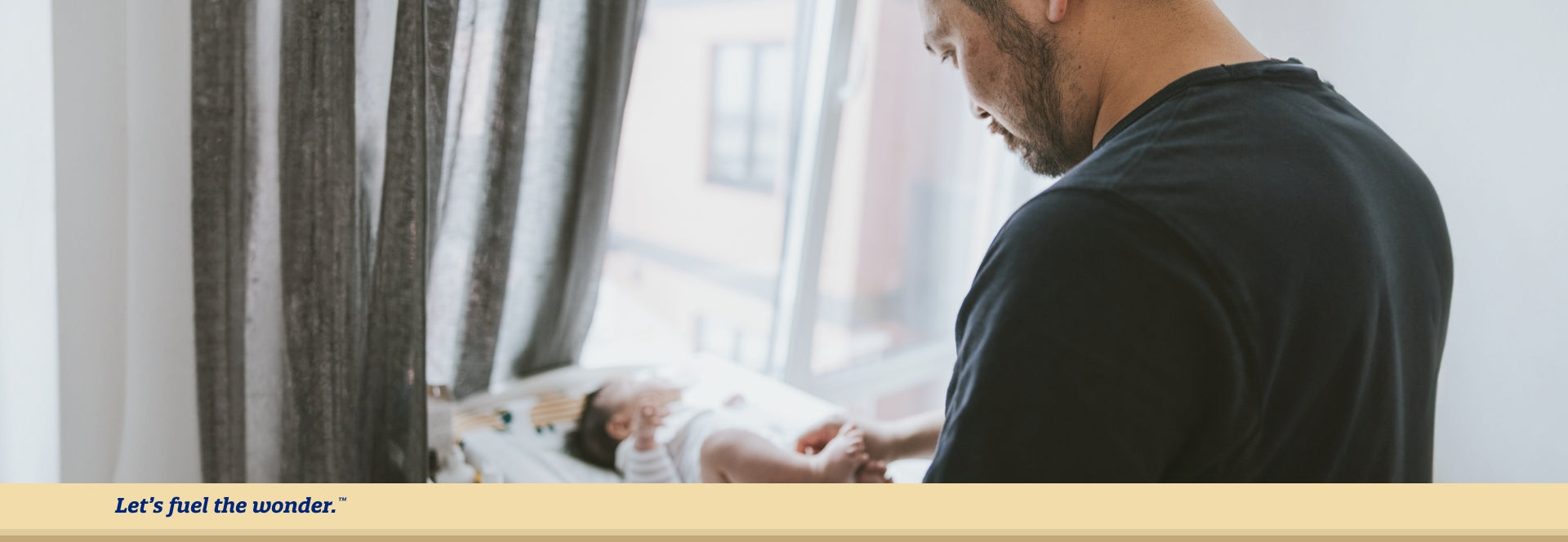 Father looking down at newborn baby and changing baby's diaper as baby is laying down on diaper changing station