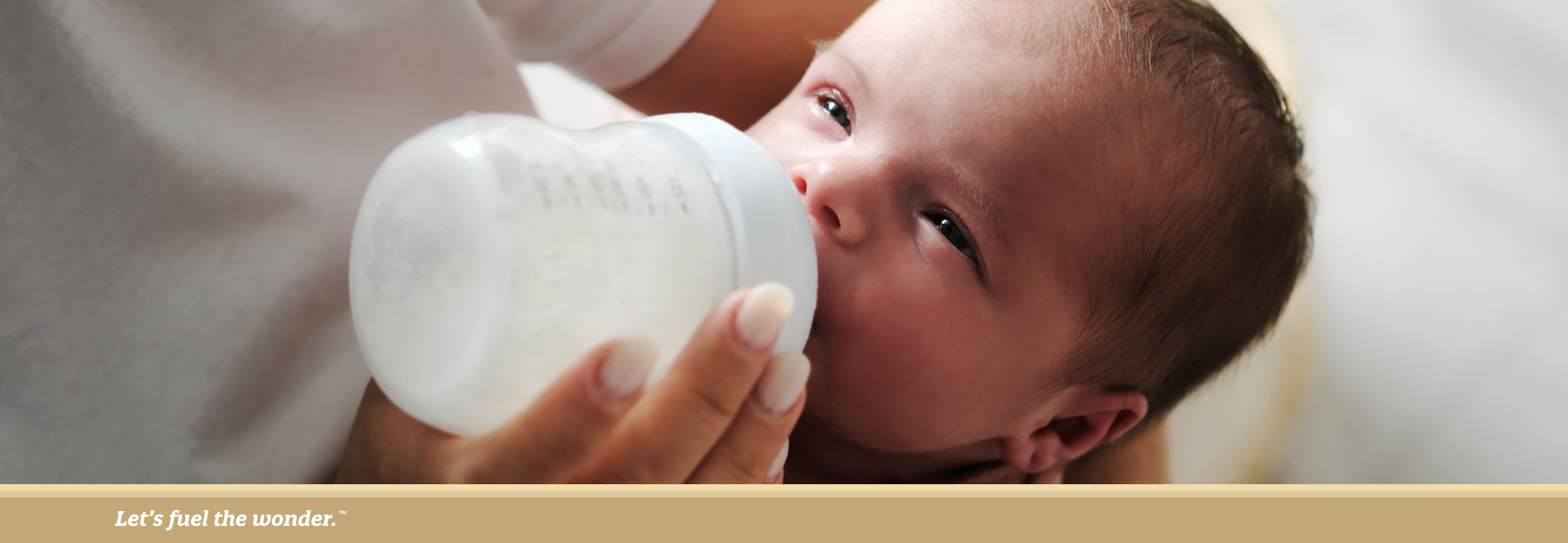 Newborn baby wrapped in a blanket being bottle-fed while resting in an adult’s arms