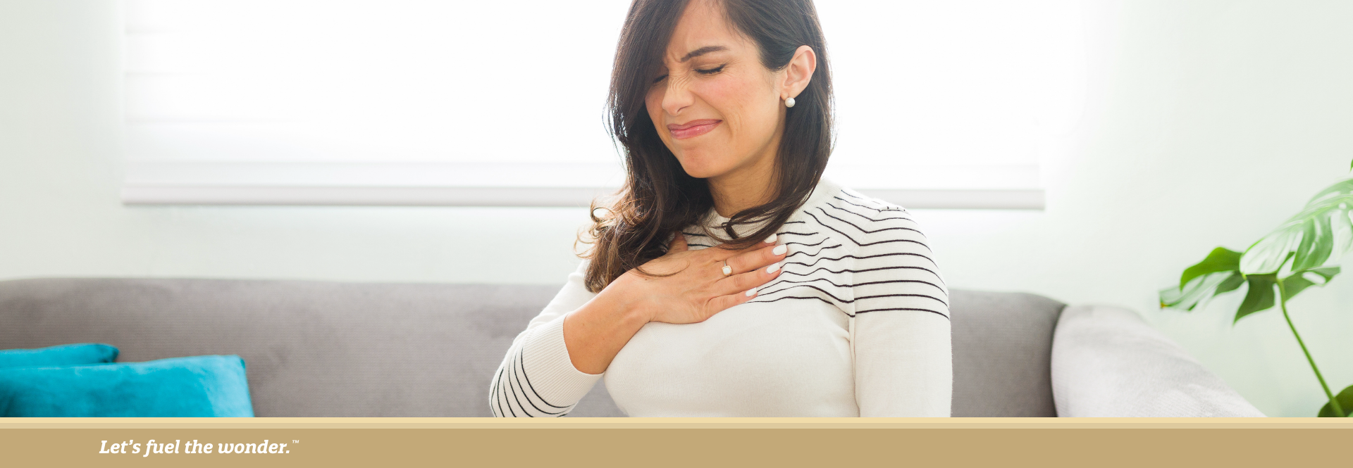 Pregnant woman sitting on a couch, holding her chest with a pained expression.