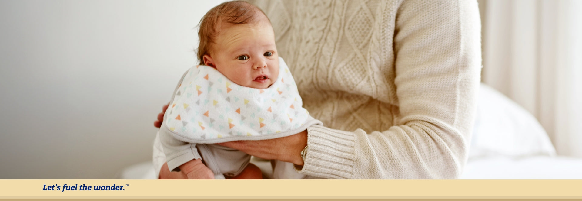 Worried baby wearing bib hunched over on mother's lap and held by mother's left hand. Mother's right hand is placed on worried baby's back.