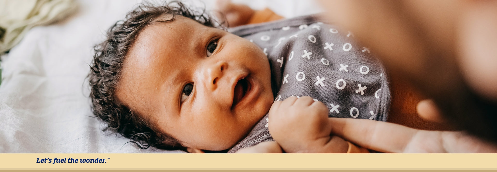 Smiling baby looking up at parent while laying down on bed and  grasping at parent's finger