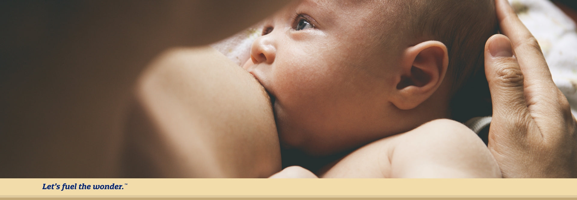 Baby breastfeeding from parents nipple while being held in breastfeeding parent's arms. Baby is looking off to their right as they are breastfeeding.