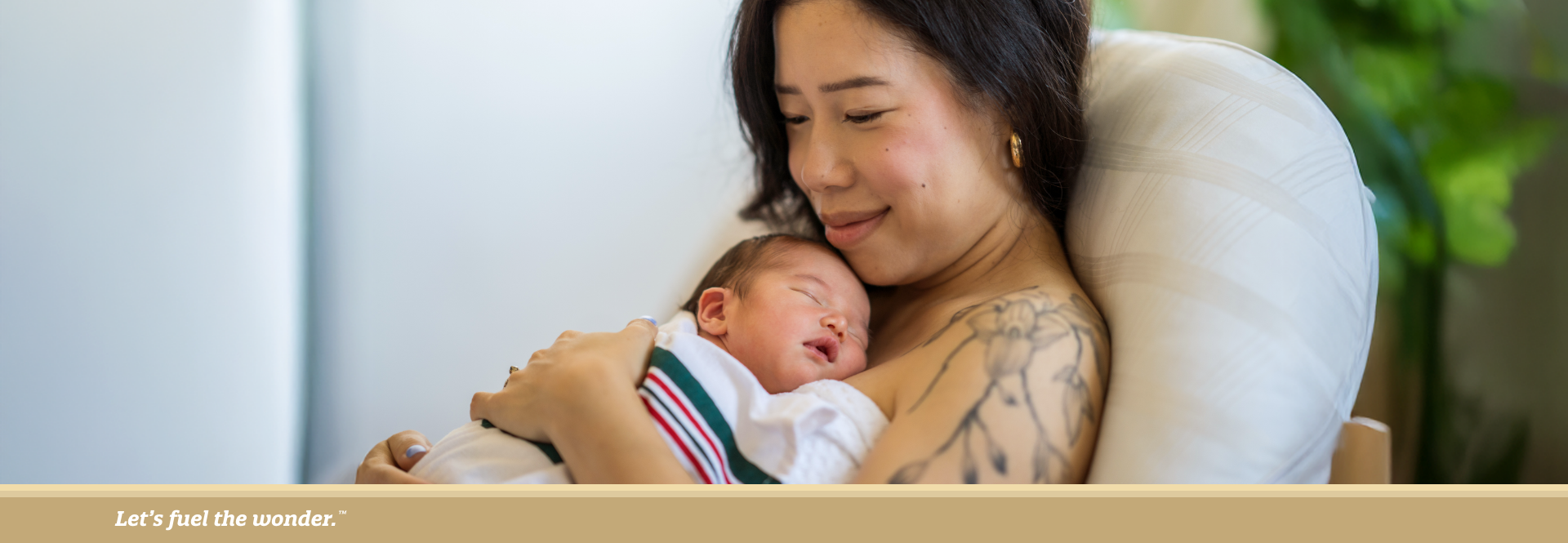 Mother cuddling her sleeping newborn, smiling gently while seated on a couch.