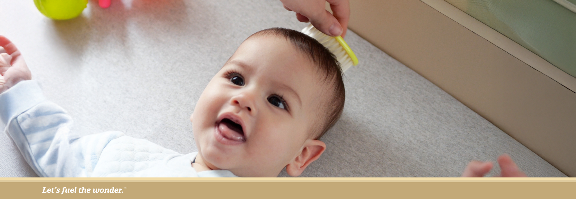 Smiling baby lying down while an adult gently brushes their hair.