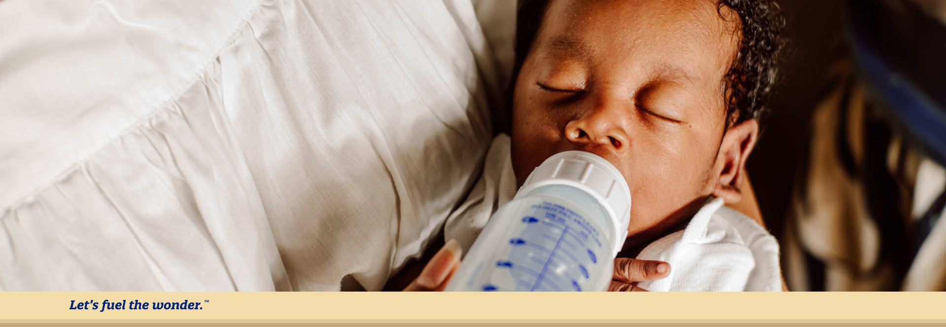 Baby with eyes closed being fed from a bottle while parent is holding baby in parent's arms