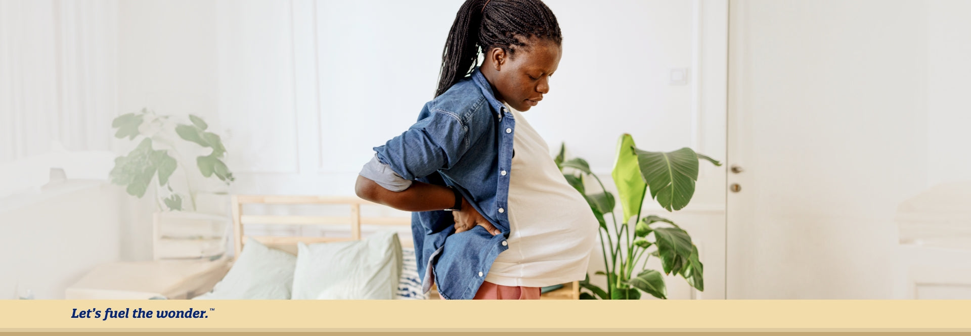 Pregnant parent standing up while supporting their back with their arm