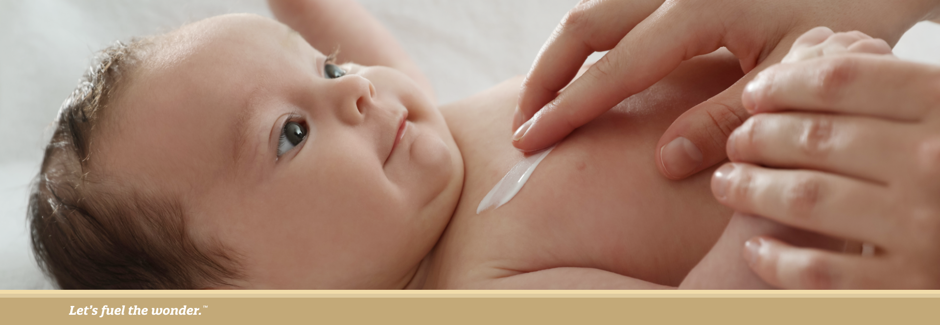 Caregiver applying lotion to a smiling baby’s chest while lying on a soft surface.