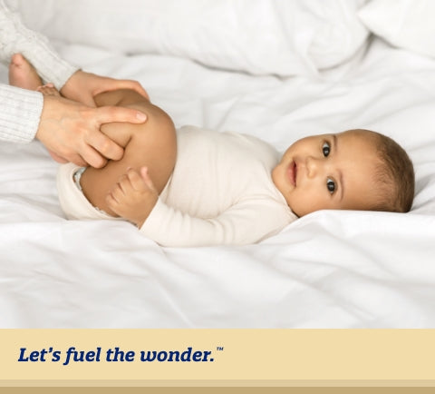 baby laying on back in bed while parent is holding baby's legs up and together to help with gas