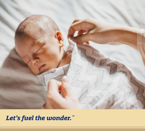 sleeping baby laying on bed while parent places swaddle around baby