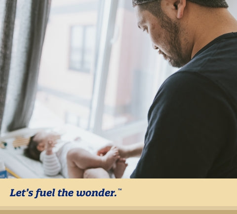 Father looking down at newborn baby and changing baby's diaper as baby is laying down on diaper changing station