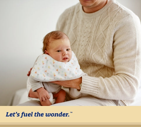 Worried baby wearing bib hunched over on mother's lap and held  by mother's left hand. Mother's right hand is placed on worried  baby's back