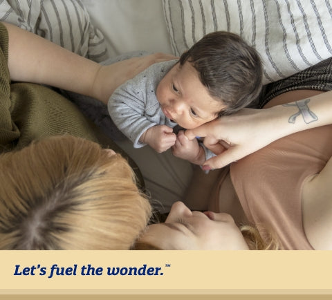 Partners laying in bed playing with sitting baby