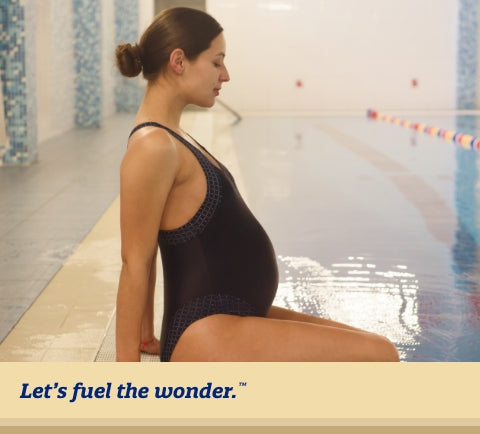 Pregnant woman with their eyes closed in a swimsuit, sitting at edge of a pool with their legs dipped into the pool water