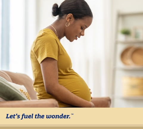 Pregnant parent looking down at pregnant belly while sitting on couch upright