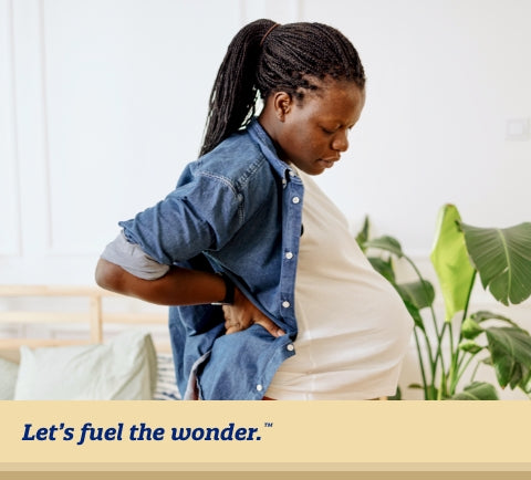 Pregnant parent standing up while supporting their back with their arm